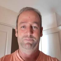 Homem de meia-idade com cabelo grisalho curto e barba rala usando uma camiseta cor pêssego.